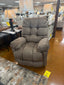 The Brosmer Cafe Recliner 9MW87-1-20866 by Best Home Furnishings, featuring an inviting brown finish, an overstuffed back, and adjustable lumbar support, is showcased in a furniture store among tables, lamps, and other items. A yellow price tag lies on the floor beside the chair.