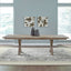 A Liberty Furniture Brentwood Table and 6 Chairs 789-C6501S-P4402-T4402 double pedestal dining table with an X-frame base and two dark vases on top, centered on a patterned area rug.