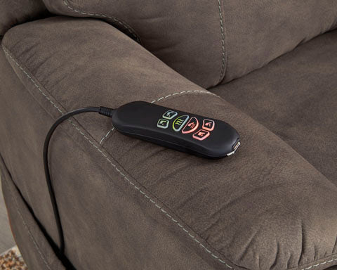 A handheld remote with glowing, multicolored buttons resting on the arm of a dark gray faux leather Crestmeade Espresso Lift Chair 1350412.