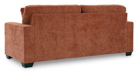 A contemporary sofa, the Ashley Aviemore Spice Sofa 2430438 is shown from the back, featuring a rust-colored fabric that evokes the warmth of burnt orange, with a plush backrest, rectangular arms, and short black legs.