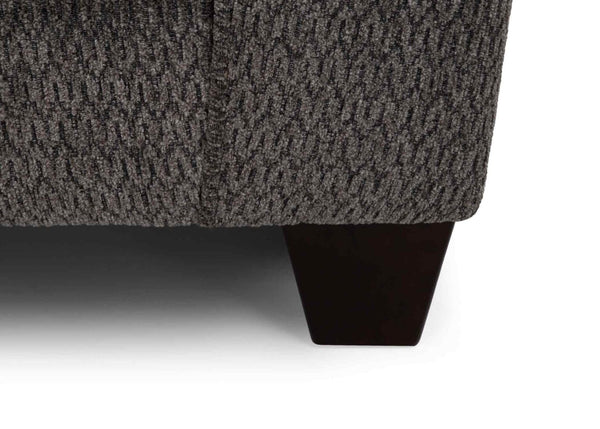 Close-up of a textured dark gray corner of the Fairmont Shasta Charcoal Sectional by Franklin Furniture Corp. (256-28-49-3403-05), highlighting the fabric pattern and one short, dark wooden leg against a white background.