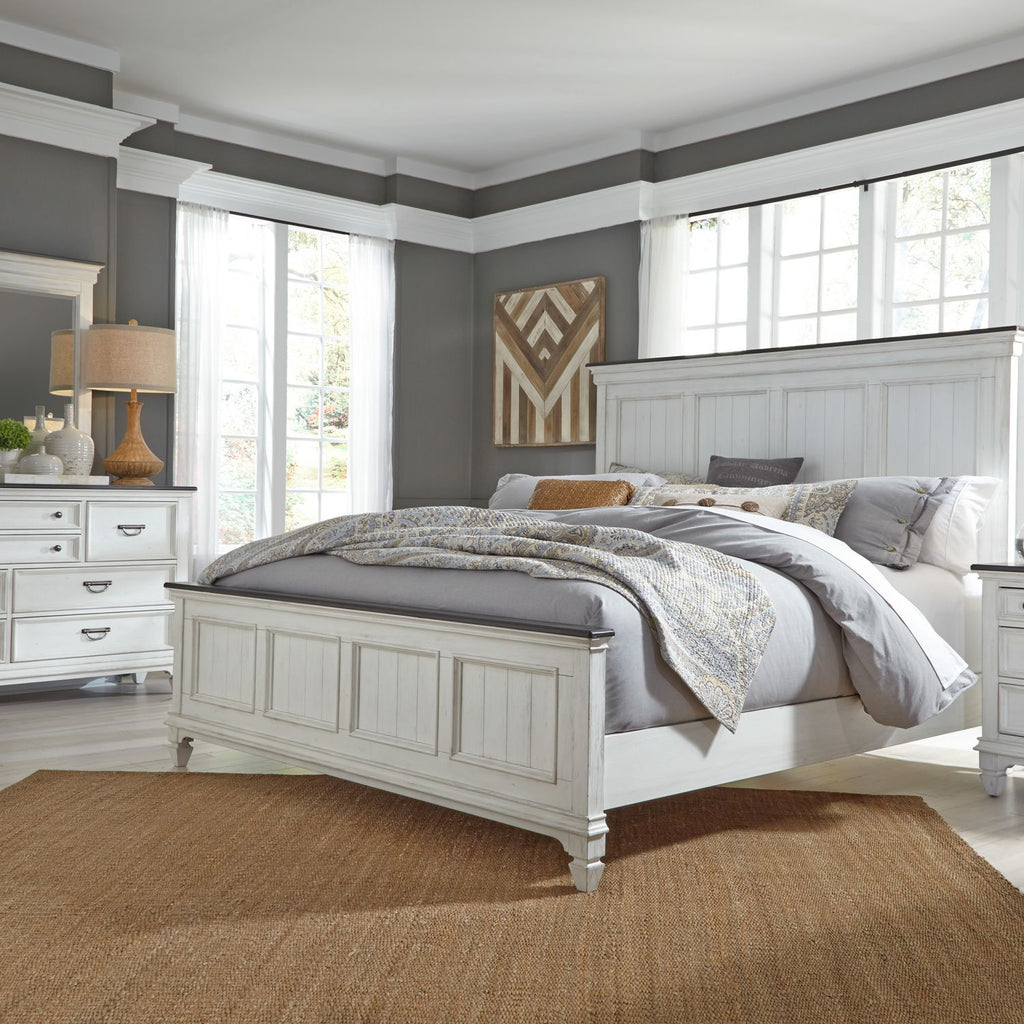 Bright bedroom with a large white bed, gray bedding, a jute rug, white dresser, nightstand, lamps, and large windows letting in natural light. Modern decor accents the clean, cozy space.