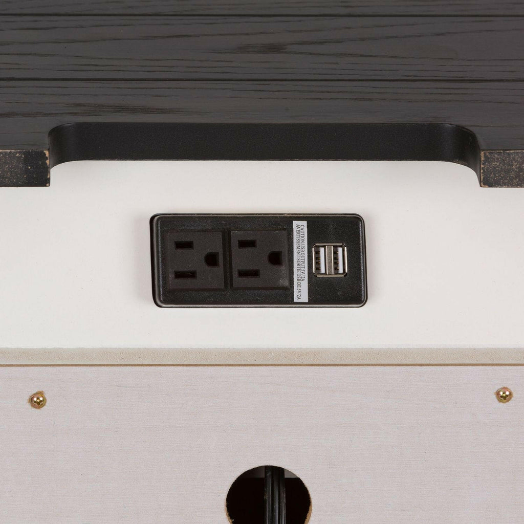 Close-up of a power outlet panel with two electrical sockets and two USB ports, mounted on a white surface with a dark wooden edge above it.