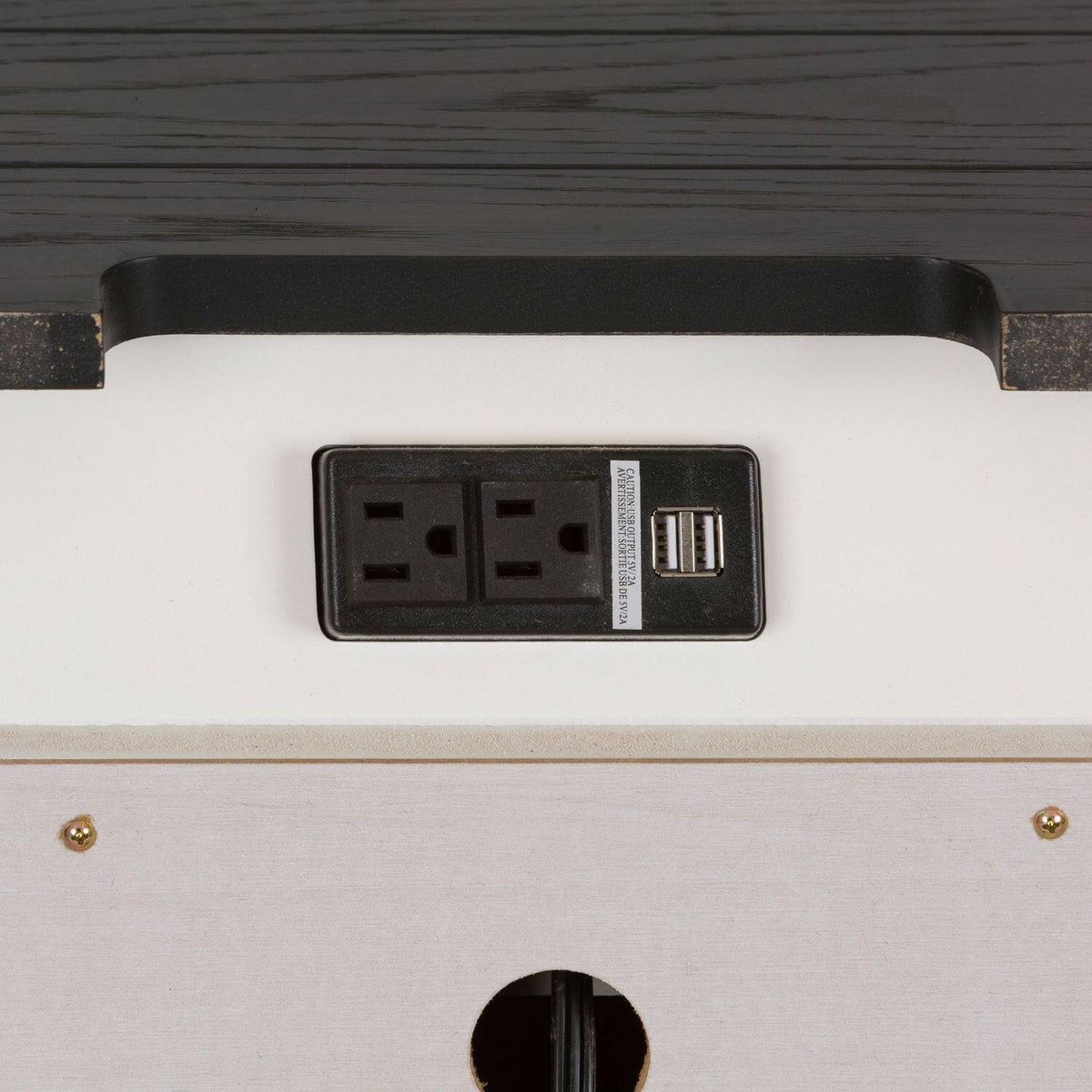 Close-up of a power outlet panel with two electrical sockets and two USB ports, mounted on a white surface with a dark wooden edge above it.