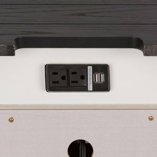 Close-up of a power outlet panel with two electrical sockets and two USB ports, mounted on a white surface with a dark wooden edge above it.