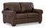 The Ashley Colleton Loveseat 5210735 showcases dark brown leather upholstery, rolled arms with nailhead trim, and two seat cushions, all set against a plain white background for a timeless traditional appeal.