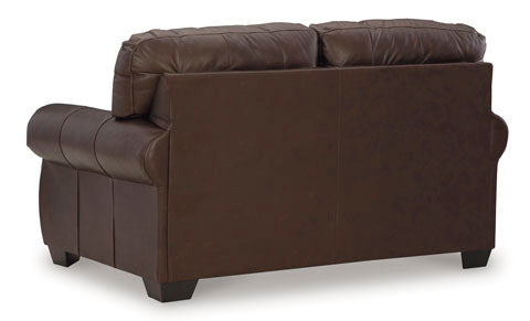 A dark brown leather Colleton Loveseat 5210735 by Ashley is viewed from the back, highlighting its cushioned armrests and backrests, with short black legs and a smooth, clean surface that embodies the classic appeal of a traditional loveseat.