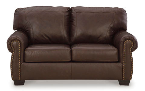 The Ashley Colleton Loveseat 5210735 is a traditional dark brown leather loveseat featuring two seat cushions, two back cushions, rolled arms, and brass nailhead trim along the front edges.