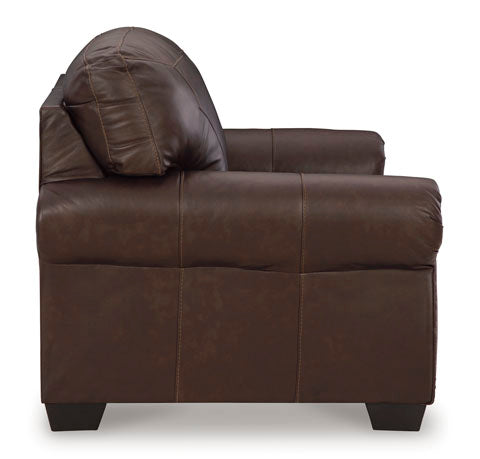 A side view of the Ashley Colleton Loveseat 5210735 in dark brown leather, featuring visible stitching and wooden legs, set against a white background.