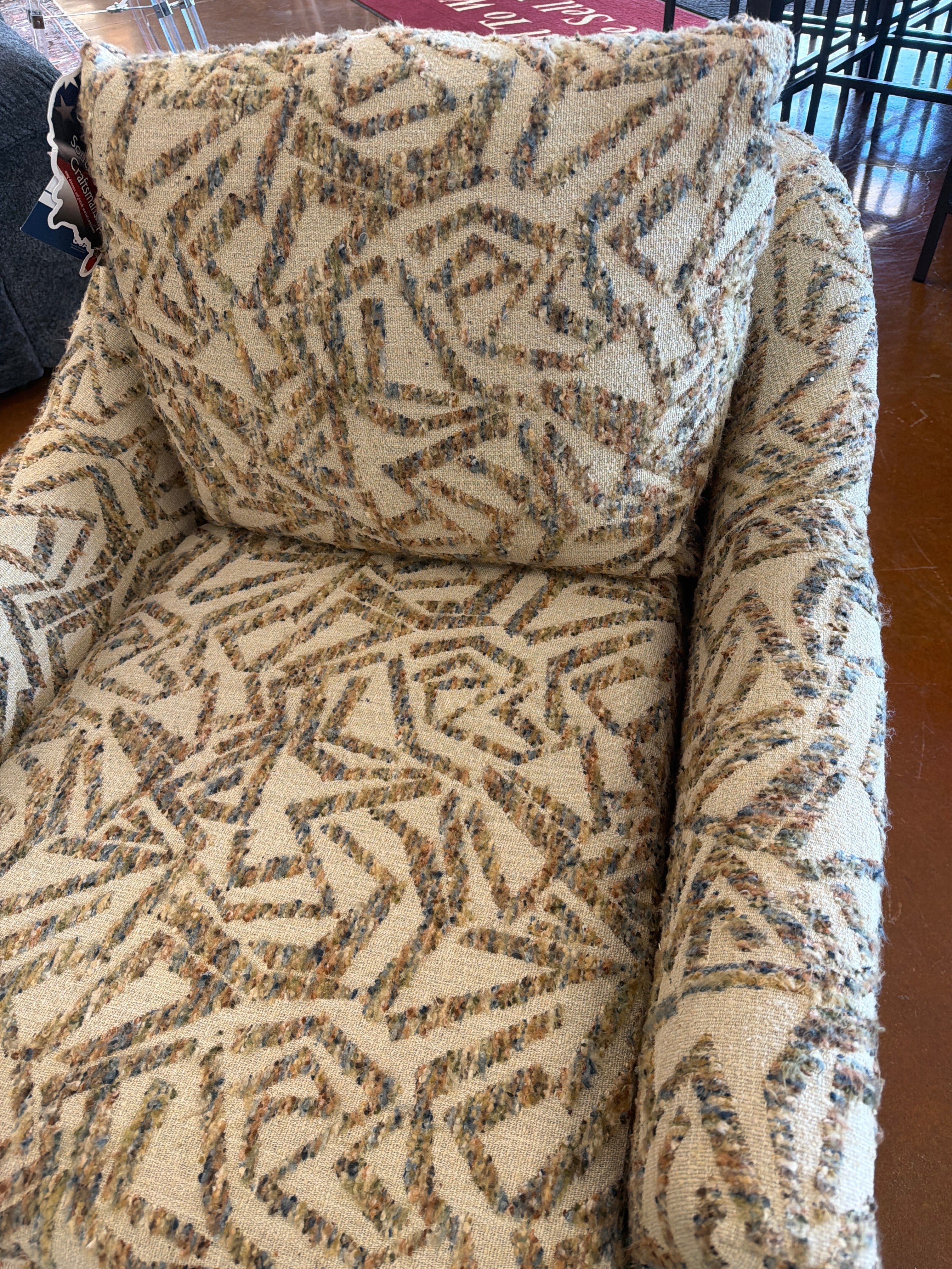 The Praslin Multi Swivel Chair 2328-35919 by Best Home Furnishings features a textured beige fabric with a geometric, abstract brown and gray pattern. Showcasing a plush pillow back for extra comfort, this barrel silhouette chair has a generously sized cushion backrest and is displayed on an indoor brown floor.