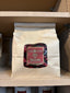 A brown paper bag labeled Circle E Firestarters Bird of Paradise by Circle E Candle sits on a wooden shelf, featuring a decorative dark red and black border around the label, reminiscent of classic Circle E Firestarters packaging.