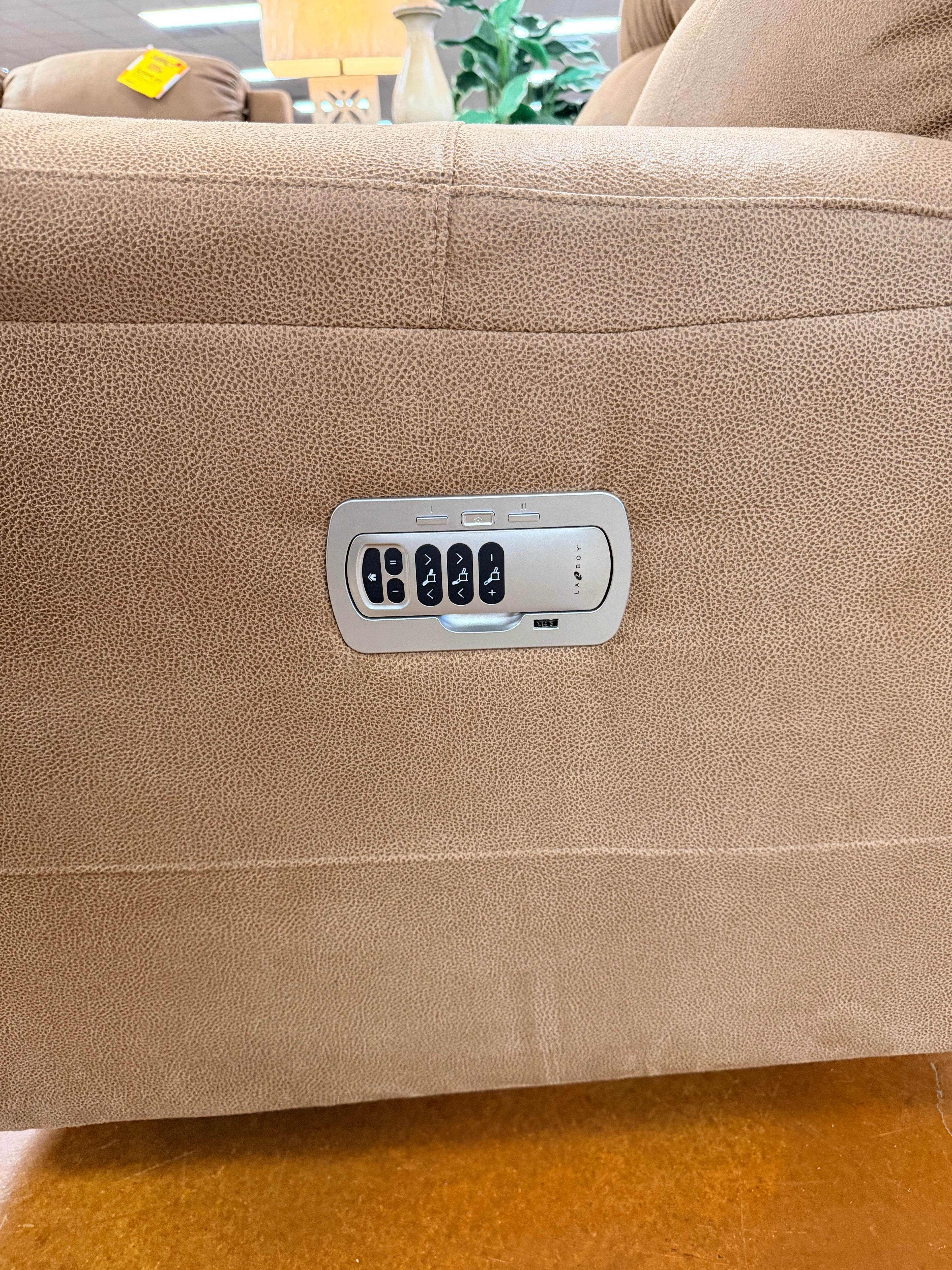 Close-up of the Dorian Power Reclining Sofa 755-X44-D1855-75, featuring a built-in control panel for adjusting seat positions, including adjustable headrest and lumbar support. Bucket chaise seats and some greenery appear in the background.
