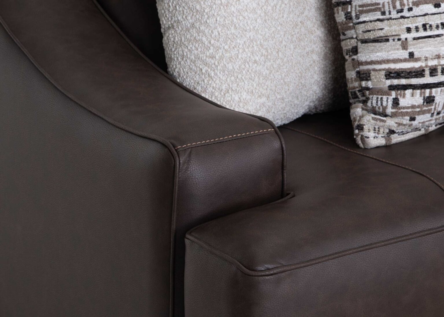 Close-up of the Prescott Duvall Coffee Loveseat by Franklin Furniture Corp., upholstered in rich dark brown leather reminiscent of premium chocolate, with beige textured and patterned decorative pillows arranged along the backrest.