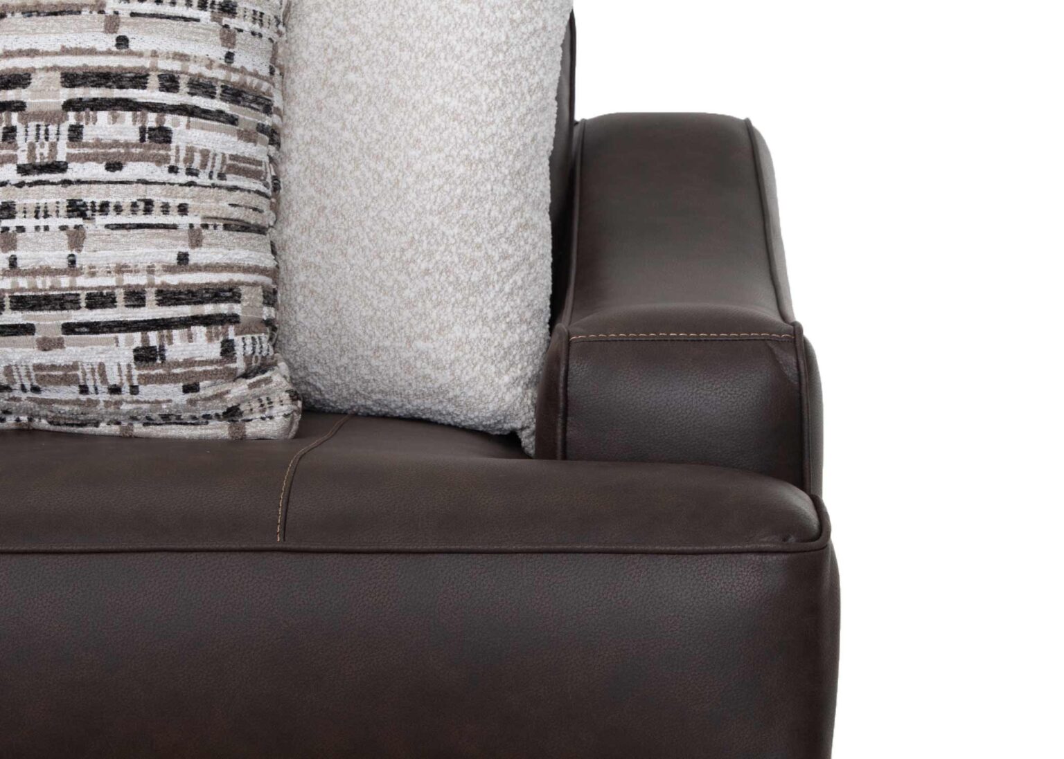 Close-up of the Franklin Furniture Corp. Prescott Duvall Coffee Sofa 89340-3429-10’s dark brown leather armrest, with two decorative pillows—one displaying a geometric black, white, and beige pattern and the other light-colored and textured—arranged neatly on the seat. The WOW Seating System guarantees exceptional comfort as a crisp white background emphasizes every detail.