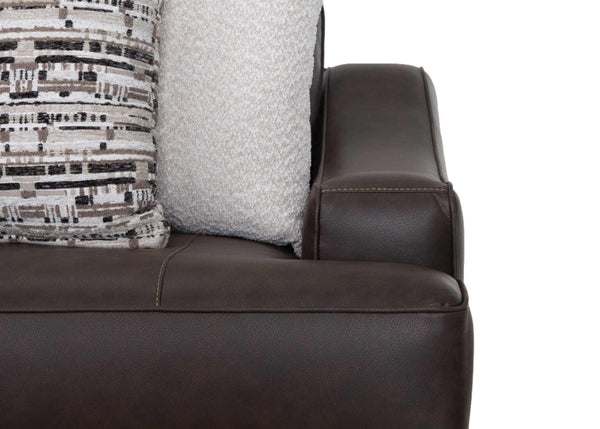 Close-up of the Franklin Furniture Corp. Prescott Duvall Coffee Sofa 89340-3429-10’s dark brown leather armrest, with two decorative pillows—one displaying a geometric black, white, and beige pattern and the other light-colored and textured—arranged neatly on the seat. The WOW Seating System guarantees exceptional comfort as a crisp white background emphasizes every detail.