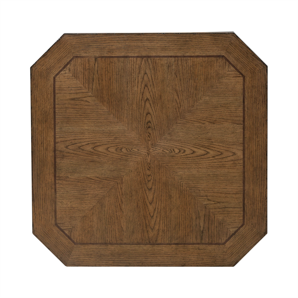 The Carolina Park Cocktail Table 930-OT1010 by Liberty Furniture features a square wooden tabletop with beveled, subtly angled corners and a symmetrical geometric wood grain pattern that radiates from the center. Its medium brown finish evokes the refined look of an elegant wood veneer coffee table.