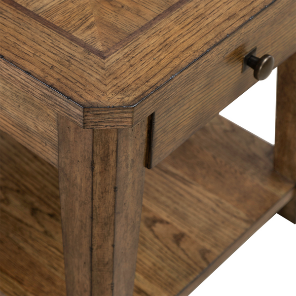 Close-up of the Liberty Furniture Carolina Park End Table 930-OT1020, featuring a storage drawer with a metal knob and a lower shelf. The white oak table showcases a natural finish with visible grain, highlighting its corner craftsmanship and surface pattern.