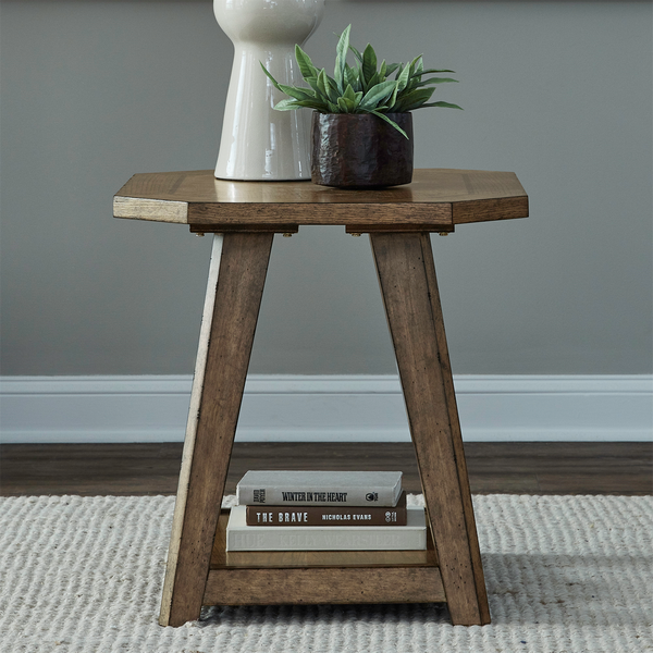 A Liberty Furniture Carolina Park End Table 930-OT1021 with angled legs holds a white vase, a green potted plant, and three stacked books on its lower shelf, set on a light textured rug against a gray wall.