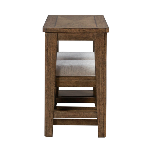 Side view of the Carolina Park Console Table and 2 Stools by Liberty Furniture, featuring a brown-stained wooden table with coordinating stools tucked beneath. Each stool has a light gray upholstered seat and a matching wood frame. Pair this set with additional upholstered seating or add bookshelf storage nearby to create a stylish and functional space.