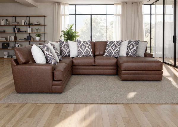 The Franklin Furniture Corp. Asheville Duvall Vintage Brown Sectional (934-04-59-69-86-3429-16) features luxurious brown leather upholstery and comes adorned with patterned and white throw pillows, arranged atop a beige rug in a bright living room with large windows, wood floors, and a bookshelf in the background. Experience unmatched comfort and timeless style with the innovative WOW Seating System built into this elegant sectional.