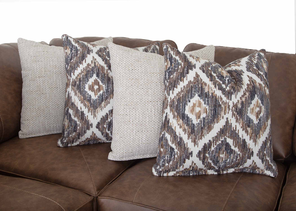 Four throw pillows are arranged on the Franklin Furniture Corp. Asheville Duvall Vintage Brown Sectional; two feature a geometric pattern in brown, beige, and gray, while the other two are a light, textured solid color.