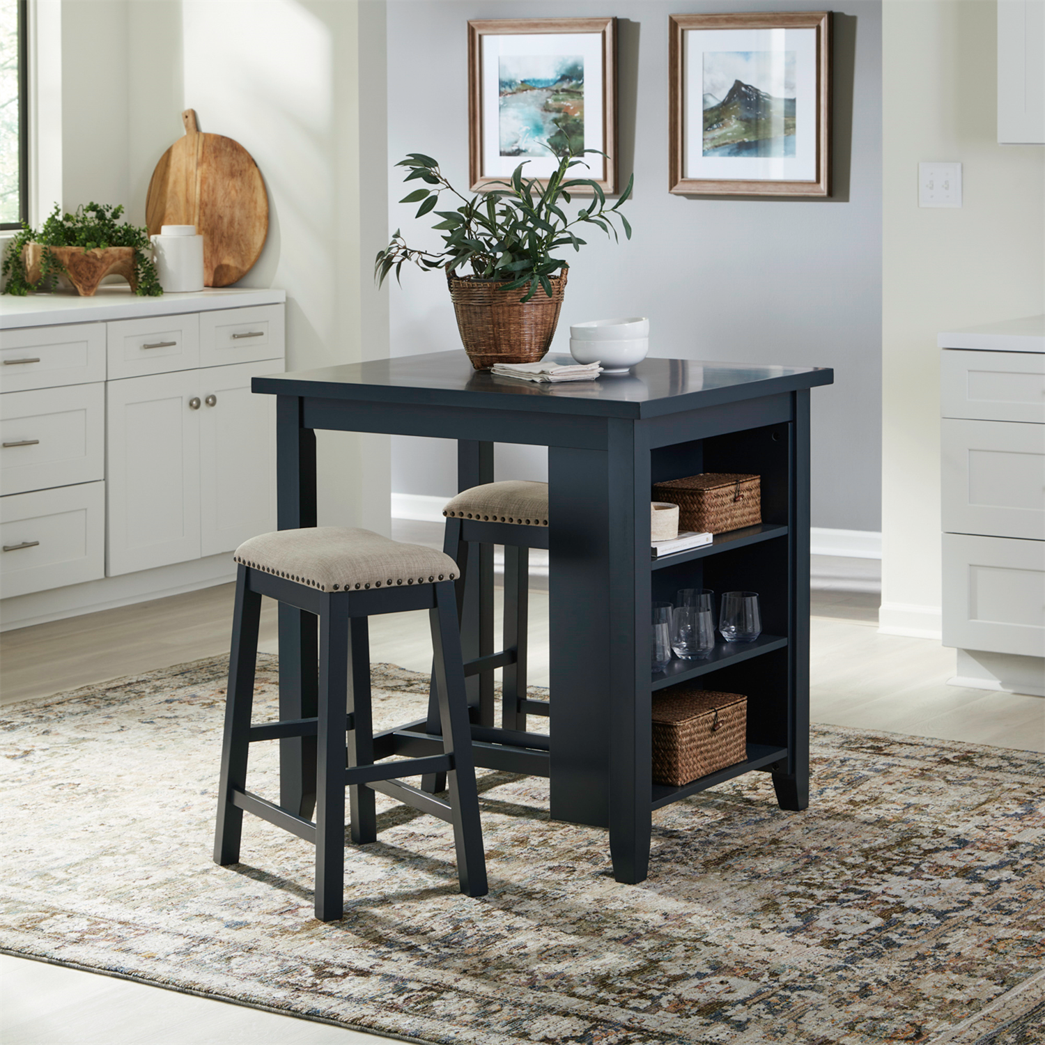 A kitchen featuring the Brook Creek Table and 2 Chairs 942NY-CD-3CTS by Liberty Furniture creates a cozy dining nook, complete with plush stools, open shelves displaying dishes, and a potted plant on the table. White cabinetry, stylish wall art, and a patterned rug enhance the bright atmosphere—making it an ideal solution for small space dining.