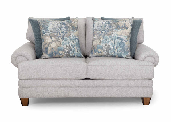 A light gray upholstered Annisa Julien Cork Loveseat (model 95720-3574-20) by Franklin Furniture Corp., featuring two large decorative pillows with blue and beige floral patterns in front of two solid blue pillows. The loveseat includes reversible seat and back cushions, rolled arms, wooden legs, and is designed for superior comfort with the WOW Seating System.