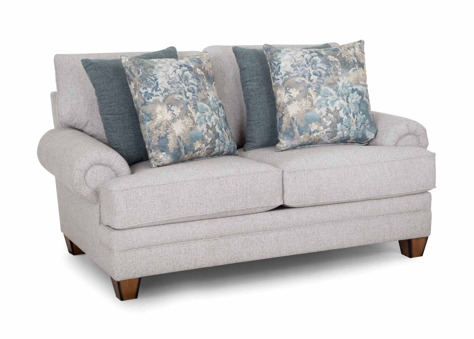 The Annisa Julien Cork Loveseat 95720-3574-20 by Franklin Furniture Corp. showcases a light gray upholstery with rolled arms, wooden legs, and the WOW Seating System. Its reversible seat and back cushions provide lasting comfort. This loveseat comes with four throw pillows—two in blue-gray and two featuring a blue floral pattern—and is displayed against a white background.