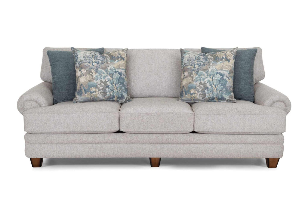 The Annisa Julien Cork Sofa 95740-3574-20 by Franklin Furniture Corp. features a light gray finish with three reversible seat cushions and sturdy wooden legs, enhanced by the WOW Seating System for superior comfort. This sofa includes four accent pillows—two in a blue floral design and two in solid blue—displayed against a plain white backdrop.