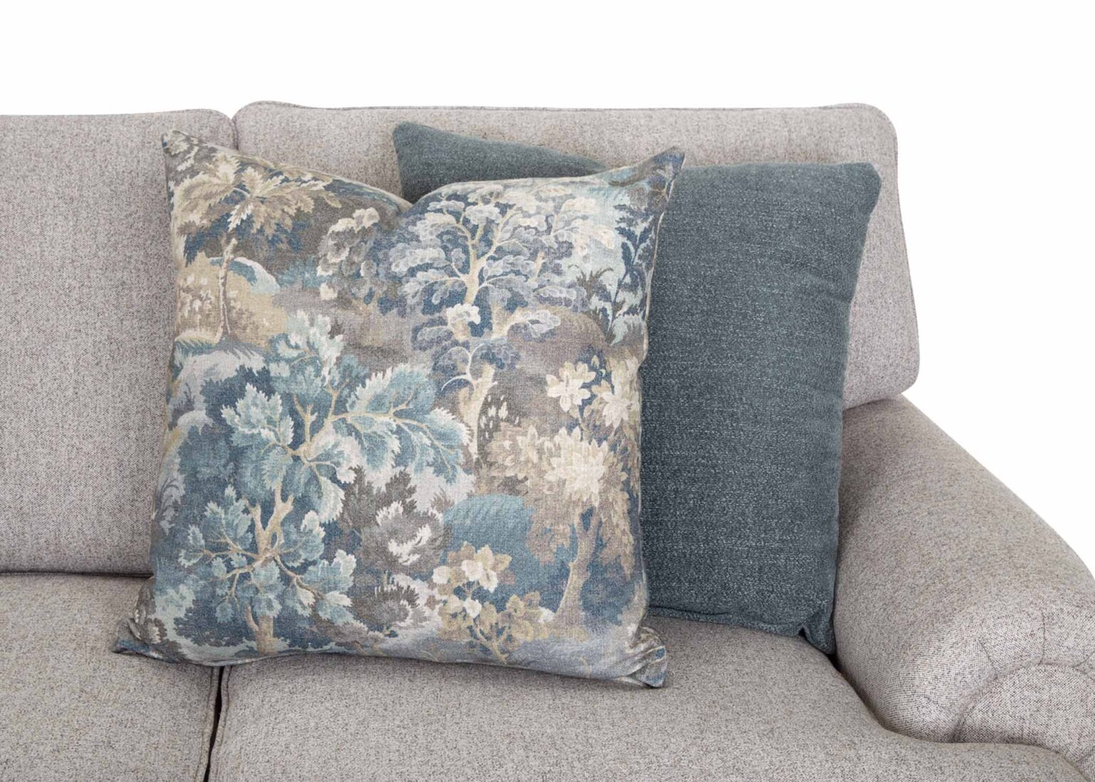 Two decorative pillows rest on a light gray Annisa Julien Cork Sofa 95740-3574-20 by Franklin Furniture Corp. One pillow showcases a blue, gray, and beige floral pattern, while the other is a solid dark grayish blue. Set against a plain white background, the image accentuates the sofa’s contemporary style and luxurious WOW Seating System comfort.