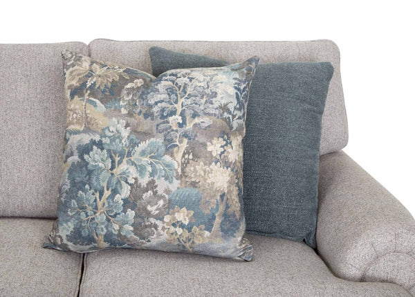 Two decorative pillows rest on a light gray Annisa Julien Cork Sofa 95740-3574-20 by Franklin Furniture Corp. One pillow showcases a blue, gray, and beige floral pattern, while the other is a solid dark grayish blue. Set against a plain white background, the image accentuates the sofa’s contemporary style and luxurious WOW Seating System comfort.