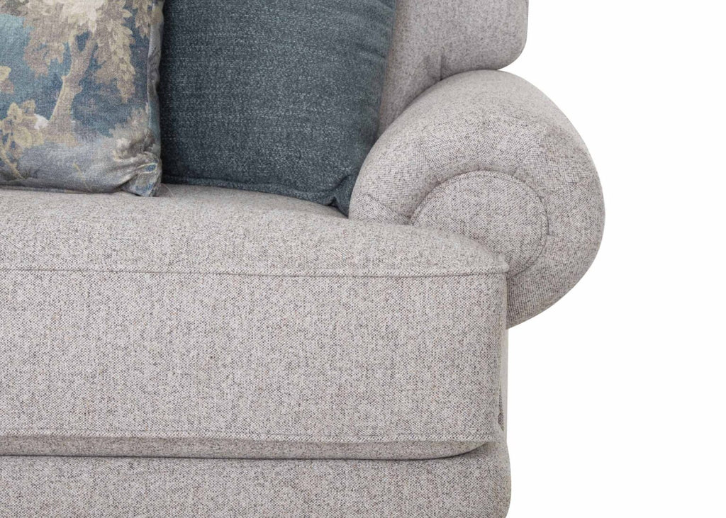 Close-up of a light gray upholstered arm of the Franklin Furniture Corp. Annisa Julien Cork Sofa 95740-3574-20, showcasing its rounded rolled design. The sofa features two cushions—one in solid blue and the other with a floral pattern—set against a white background. Reversible seat cushions add versatility and enhanced comfort to this piece.
