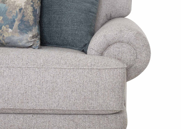 Close-up of a light gray upholstered arm of the Franklin Furniture Corp. Annisa Julien Cork Sofa 95740-3574-20, showcasing its rounded rolled design. The sofa features two cushions—one in solid blue and the other with a floral pattern—set against a white background. Reversible seat cushions add versatility and enhanced comfort to this piece.