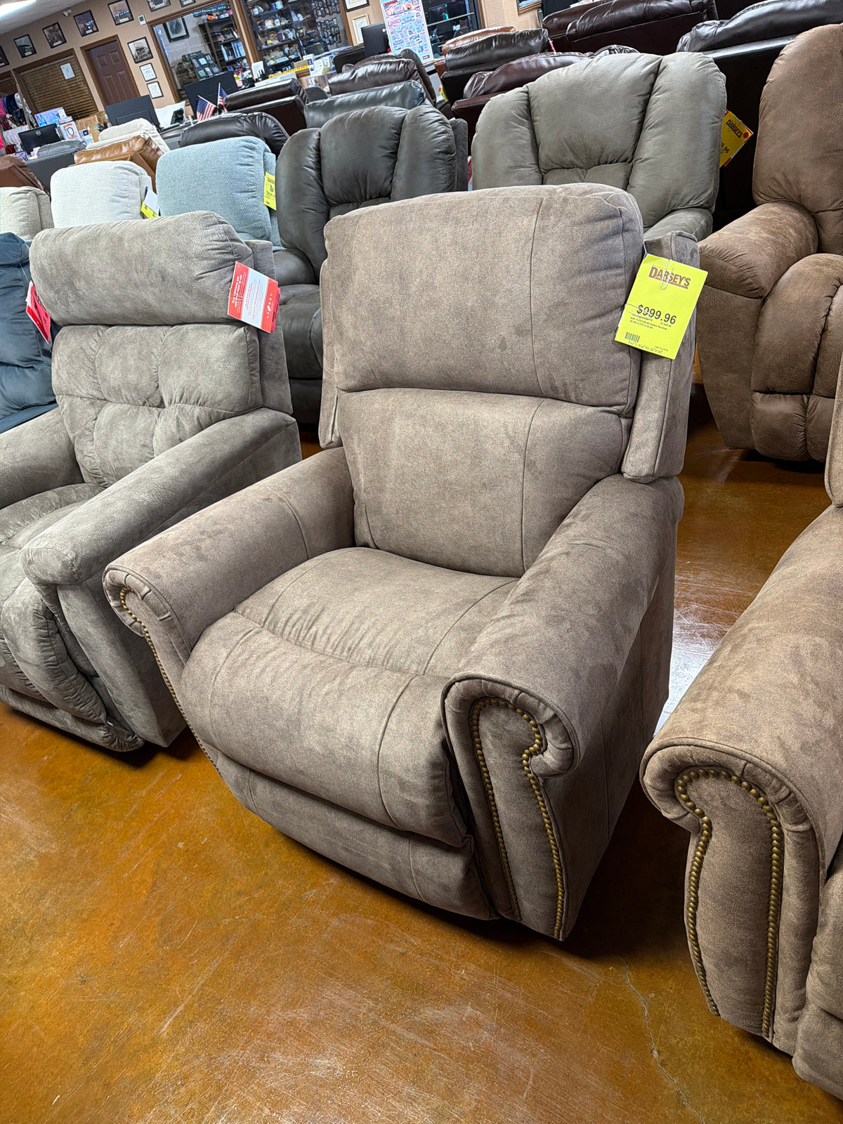 A taupe La-Z-Boy Dutton Recliner 828-10-D2128-69 with nailhead trim on the arms, displayed in a furniture showroom with a price tag attached. Main image