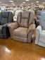 A La-Z-Boy Jasper Recliner (model 709-10-D1825-74) in brown upholstery is showcased in a furniture showroom, surrounded by other wide-seat recliners in different colors. The glossy brown floor and framed artwork on the walls provide a backdrop that complements the chair’s ultra-plush chaise seat.