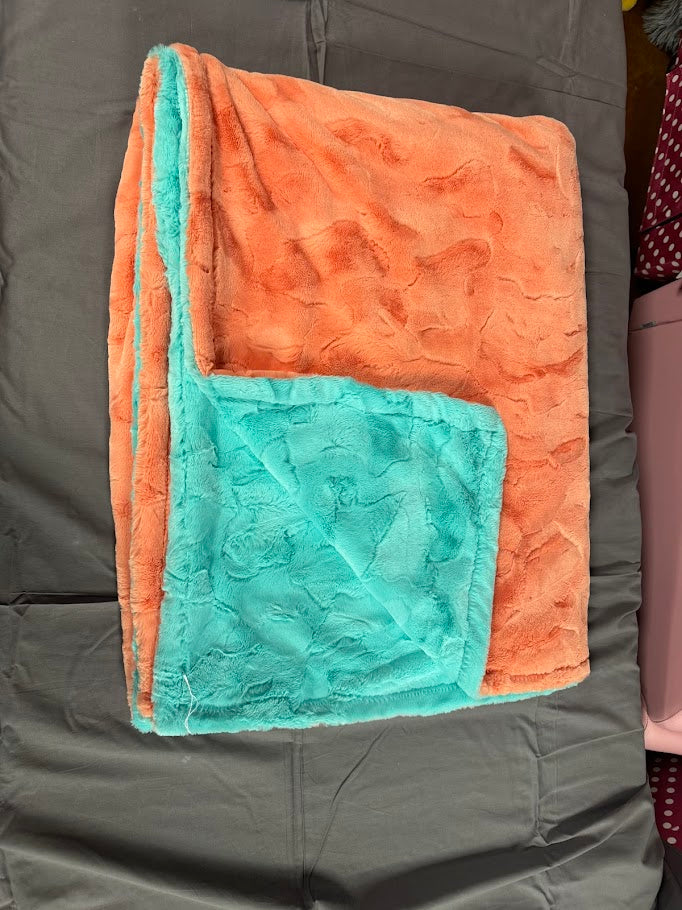 Folded blanket with orange and teal pattern on a dark surface
