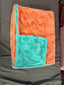Folded blanket with orange and teal pattern on a dark surface