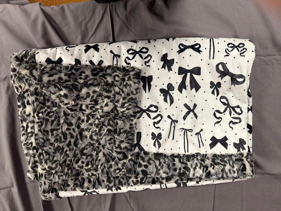 Two patterned blankets, one with a leopard print and the other with black bows on a gray surface.