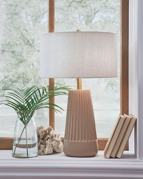 A contemporary Ashley Dellner Lamp L100854 with a reeded, tapered base and a light-colored drum shade, sitting on a windowsill next to a glass vase with greenery, a piece of coral, and two books.