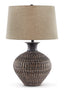 The Ashley Magan Lamp L207354 features a textured, round ceramic base with a bronze-tone finish and is topped with a wide beige fabric lampshade.