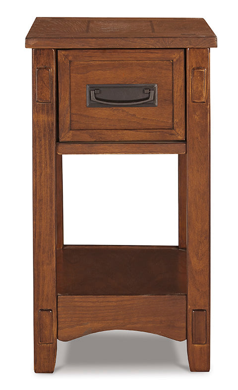 The Ashley Breegin Brown Chairside End Table T007-319 is a tall, narrow Mission-style end table in brown wood, featuring one top drawer with a dark metal pull and an open storage shelf at the bottom.