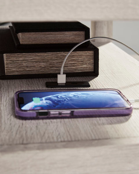 A light-colored Fendenmore White Chairside End Table T190-217 with a charging smartphone and a stack of two books on its surface.