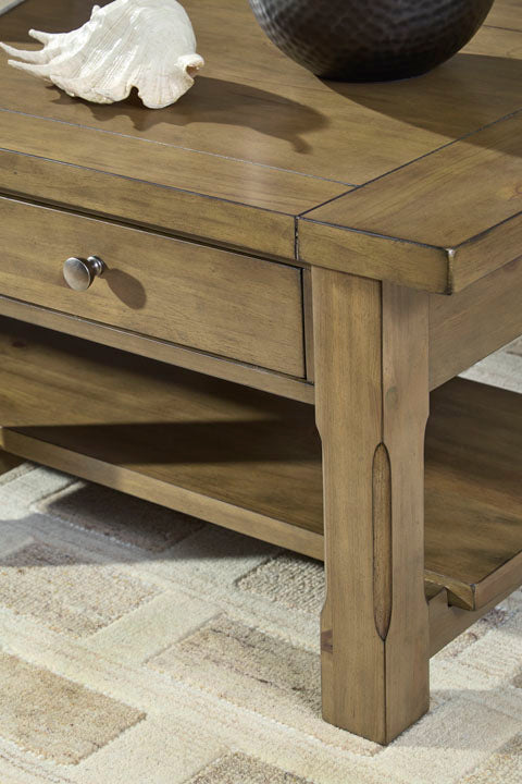 Close-up of the Ashley Vandenmore Coffee Table T539-1, a farmhouse-style wooden table featuring a convenient drawer with a silver knob and topped with a decorative seashell, displayed on a beige patterned rug for enhanced storage and style.