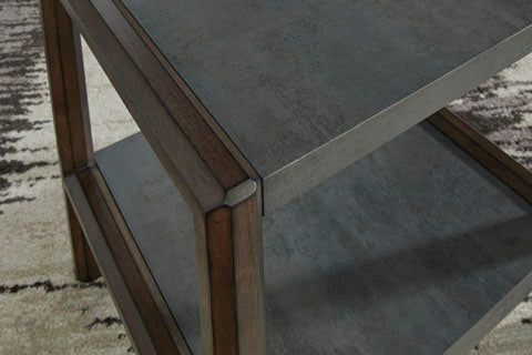 A close-up of the Ashley Kallenny End Table T669-3, showcasing its two-tiered mixed-material design with a metal top and shelf, wooden frame, and a patterned beige and brown carpet underneath.
