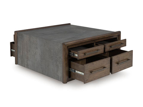 The Ashley Kallenny Cocktail Table (T669-8) features a rectangular design with a concrete-style top and wooden frame, showcasing industrial flair through its four open drawers equipped with metal handles and exposed side tracks.