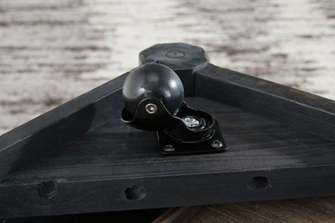 A close-up of a black caster ball wheel attached to the corner of the Ashley Kallenny Cocktail Table T669-8, set against a light-colored, textured backdrop that accentuates the table’s subtle industrial edge.