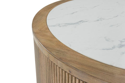 A close-up of the Ashley Camdill Coffee Table (T808-8) highlights its contemporary round design, featuring a wood base with vertical grooves and a smooth white faux Carrara marble top accented by light gray veining.