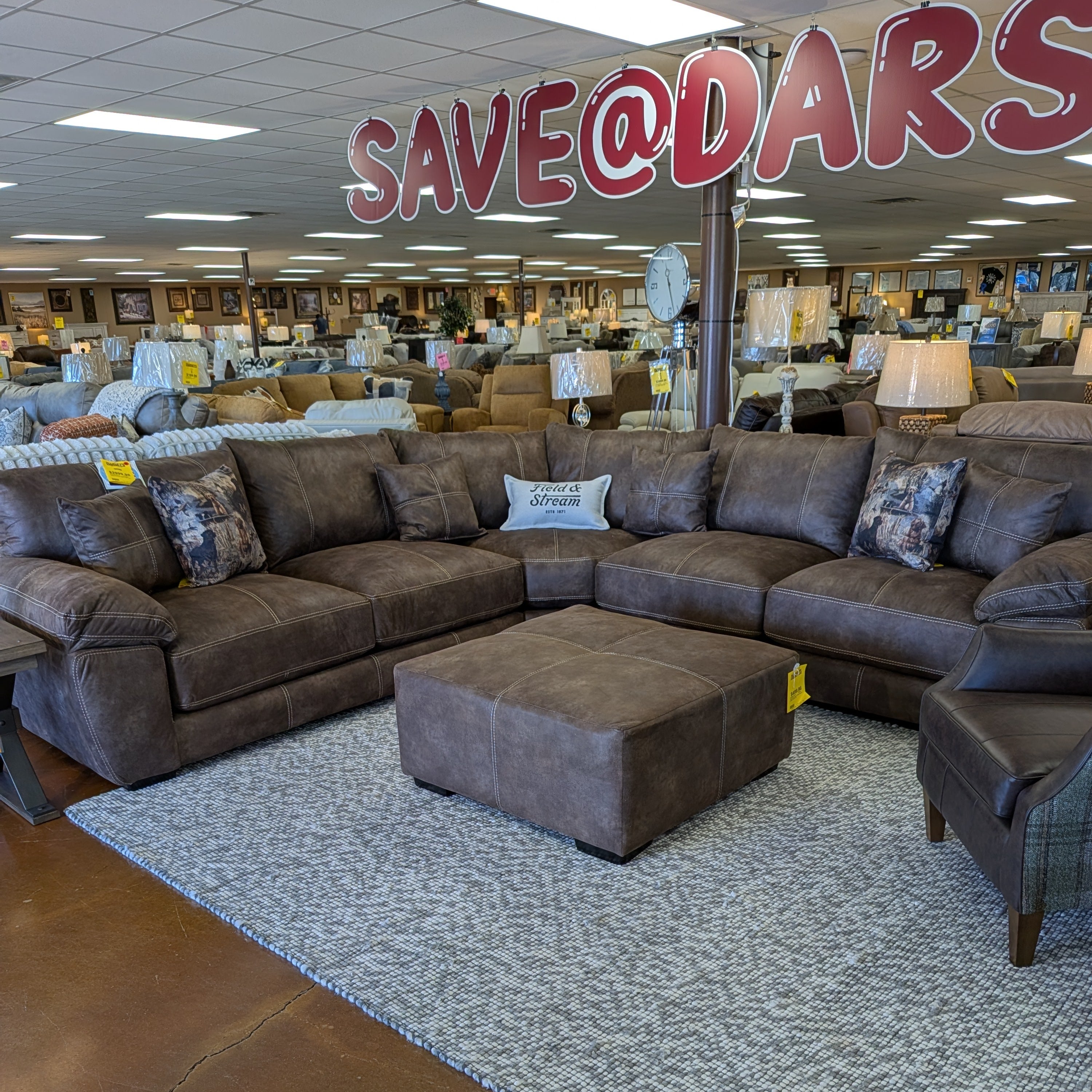 Sectional sofa with ottoman in a furniture store with 'SAVE@dars' sign.