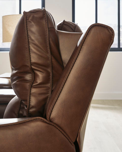 Close-up side view of the Ashley DeepWakes Canyon Power Recliner U6260713, crafted in top grain leather, highlighting its adjustable backrest and extended footrest in a bright room with large windows and a lamp in the background.