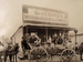 Old black-and-white photo of people and horses in front of a wooden store labeled “GEO. E. DAPSEY. DRY GOODS, GROCERIES & FURNITURE.” A wagon is parked in front.